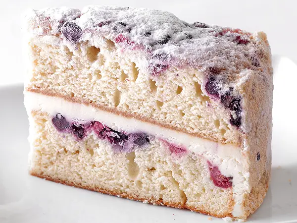 Sysco Exclusive Lemon Berry Mascarpone Cake topped with blueberries, cranberries, vanilla crumb, and powdered sugar with layers of lemon cream filling.